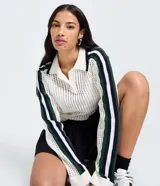 Blusa de punto perforado color blanco, con cuello polo y cierre parcial de botones. Presenta mangas largas con rayas contrastantes en azul marino y verde.