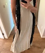 Vestido largo de estilo lencero color crema, con puntillas negras aplicadas verticalmente en el frente y la espalda.