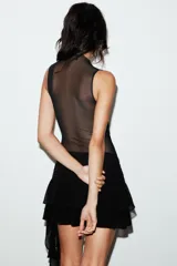 Falda pantalón negra de tiro bajo con cintura drapeada y bajo acabado en volantes superpuestos. Presenta un lazo largo y fino que cae desde el lateral.