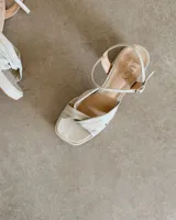 Sandalia de cuero vacuno color dorado, con plataforma y taco cuadrado. Presenta una tira delgada en el tobillo y detalle de nudo en la capellada.