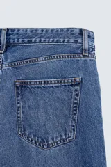 Pantalón de jean celeste de corte flare, con tiro medio, cinco bolsillos, cierre frontal con cremallera y botón, y bajo con acabado irregular.