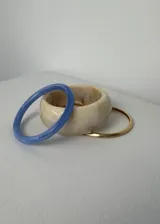 Pack de tres pulseras rígidas de diferentes materiales y colores: una azul traslúcida, una beige marmolada y una dorada.