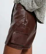 Short pollera femenino de PU color marrón oscuro, con cintura con trabillas, cierre frontal y bolsillos cargo laterales.
