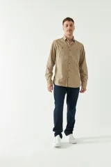 Camisa de gabardina color beige, de corte slim fit, con mangas largas, cartera abotonada y bolsillos en el pecho.