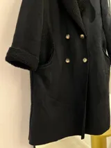 Tapado largo negro de gamuza con interior de corderito. Tiene detalles de corderito visible en cuello y bolsillos, y cierre frontal con botones.