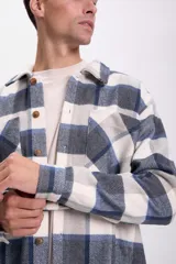 Sobrecamisa de franela a cuadros azul marino, gris y blanco, con cuello clásico, cierre frontal con botones, dos bolsillos de parche en el pecho y mangas largas con puños abotonados.