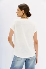 Remera blanca de lino con calce al cuerpo y mangas cortas. Presenta bordados de lentejuelas y mostacillas en los hombros.