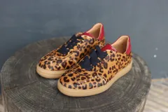 Zapatillas bajas con capellada de animal print, cordones negros y detalles en rojo en el talón.