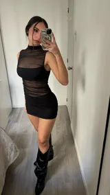 Minivestido negro ajustado al cuerpo, con cuello alto de mesh transparente y botas negras de caña alta.