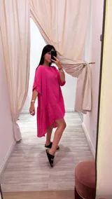 Vestido corto color fucsia, de lino, con cuello redondo y mangas cortas. Es más corto adelante que atrás, con corte transversal en la falda.