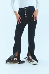 Pantalón de jean azul de tiro medio alto, corte oxford con botamanga ancha y tajo lateral. Cierre frontal con cinco botones metálicos.