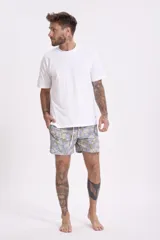 Short de baño para hombre, color celeste pálido, con estampado floral en tonos crema y verde oliva. Presenta cordón de ajuste blanco en la cintura y bolsillos laterales.