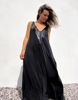 Vestido largo negro con escote en V y breteles finos. Presenta apliques de lentejuelas negras en el escote.