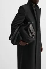 Bolso tipo shopper negro fabricado en tejido de algodón con asas de piel. Cuenta con dos bolsillos laterales exteriores y un bolsillo interno.