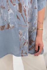 Blusa celeste con estampado de hojas marrones, cuello en V con terminación desflecada y mangas cortas.