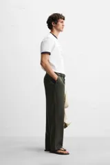 Pantalón verde oscuro de corte amplio confeccionado en tejido de lyocell. Presenta pliegues frontales, bolsillos laterales y traseros de ojal. Cierre frontal con cremallera y botón.
