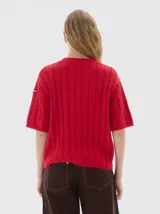 Remera de punto negra con cuello redondo y mangas cortas. Presenta un diseño de tejido con trenzas verticales.