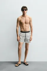 Bañador corto de hombre con estampado a rayas horizontales blancas y negras. Tiene cintura elástica ajustable con cordón, bolsillos laterales y trasero.