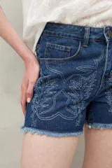 Short de jean azul con bordado floral en el frente y ruedo desflecado.