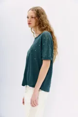Remera blanca de lino con tachas plateadas en el frente, cuello redondo y mangas cortas.