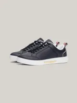 Zapatillas Tommy Hilfiger de cuero azul marino con suela blanca, cordones negros, interior blanco y detalles dorados en el talón y en el lateral.