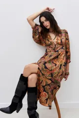 Vestido midi con estampado de mariposas en tonos naranja, verde y negro. Tiene escote en V, mangas largas abullonadas y abertura lateral en la falda.