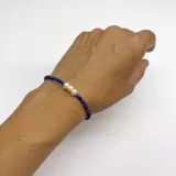 Pulsera elaborada con mini cuentas facetadas de Lapislázuli y tres Perlas de Río en el centro. Las terminaciones son en acero con baño de oro y cuenta con un dije de nácar.