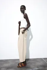 Pantalón color beige de tiro alto, corte ancho y largo midi, con pinzas delanteras, bolsillos laterales y traseros. Cierre frontal con cremallera y botón.