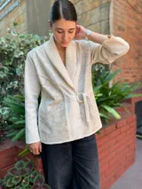 Chaqueta color crema con cuello tipo chal, cierre cruzado con cinturón y bolsillos laterales.
