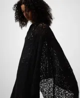 Capa de punto cardado en color negro con diseño asimétrico y bordado calado. Presenta escote redondeado y aberturas laterales. Confeccionada en una mezcla de mohair y lyocell que aporta suavidad y ligereza.