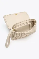 Bolso alargado color beige con diseño trenzado, asa bandolera y tirador con pulsera de mano. Incluye bolsillo interior y cierre con solapa y botón imantado.