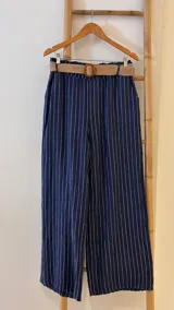 Pantalón de lino azul marino con rayas verticales blancas, corte palazzo, cintura alta con elástico y cinturón de raffia con hebilla redonda.