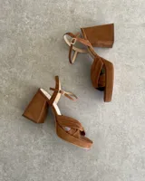 Sandalia de cuero vacuno color dorado, con plataforma y taco cuadrado. Presenta una tira delgada en el tobillo y detalle de nudo en la capellada.