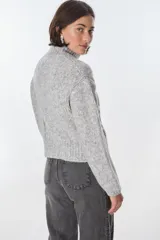 Cardigan color crudo de tejido de punto con diseño trenzado, cuello alto y cierre frontal con cremallera.