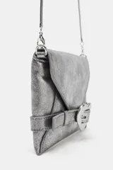 Bolso formato bandolera color plateado metalizado, con solapa frontal que simula un cinturón con hebilla metálica en forma de corazón. Posee asa fina de cadena y cierre mediante botón imantado.