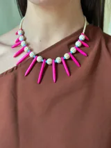 Collar corto con cuentas de cerámica color crema, pinchos de piedra reconstituida color fucsia, cristales checos color celeste y mostacillas. Se cierra con cadena de acero quirúrgico para regular el largo.