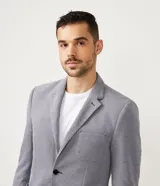Blazer masculino color gris claro, de tejido liso con textura casual, con solapas, bolsillos amplios de parche en la parte delantera y un bolsillo superior. Cierre frontal de un solo botón.