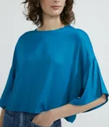 Blusa celeste de viscosa con textura satinada, cuello redondo, manga corta con sisa desplazada y abertura en la espalda.