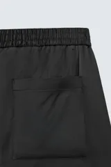 Bermuda negra de corte relajado, confeccionada en tejido satinado de viscosa. Presenta cintura elástica ajustable con cordón interior, bolsillos frontales y un bolsillo trasero de plastrón.