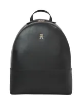 Mochila negra de poliuretano con forma redondeada en la parte superior y base rectangular. Cuenta con asa de mano superior, correas acolchadas ajustables y un logotipo metálico monograma TH en el centro.
