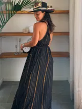 Vestido largo blanco con finas rayas verticales en lurex dorado. Presenta un escote profundo en V con tirantes finos que se anudan en la nuca (estilo halter) y un corte imperio con frunces en la cintura.