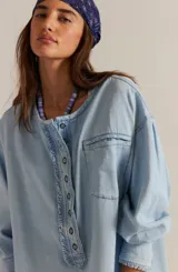 Camisa de denim chambray celeste, estilo oversized, con escote henley alargado con botones, hombros caídos y mangas abullonadas con puños terminados en volados.