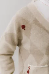Cárdigan color beige con patrón de rombos en tonos marrones, cierre con botones, bolsillos frontales y bordados de cerezas.