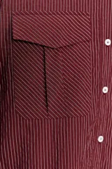 Camisa color borgoña a rayas verticales finas, de corte recto, con cuello solapa y manga larga. Tiene dos bolsillos de parche con solapa en el pecho y cierre frontal con botones.