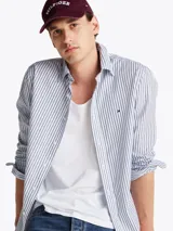 Camisa de mangas largas a rayas verticales azules y blancas, confeccionada en popelín de puro algodón con tecnología Flex que le confiere elasticidad. Tiene cuello abotonado, puños redondeados con botón y logo de Tommy Hilfiger bordado en el pecho.
