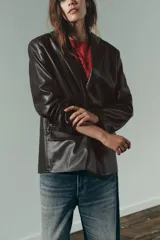 Blazer marrón oscuro de efecto piel, con cuello solapa y manga larga. Tiene bolsillos de plastrón en la parte delantera, forro interior a tono y cierre frontal con botones.