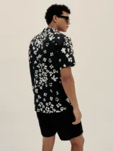 Camisa de manga corta con cuello estilo cubano y estampado floral blanco sobre fondo negro.