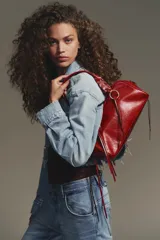 Bolso bowling color rojo con efecto craquelado. Tiene doble asa de hombro con detalles metálicos y asa bandolera extraíble. Incluye bolsillo interior con cremallera y cierre principal con cremallera.