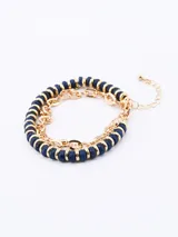 Set de tres pulseras elásticas: una de cuentas facetadas azul marino con detalles dorados, una de cuentas blancas con detalles dorados y una de cadena dorada con eslabones ovalados.