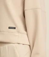 Buzo deportivo femenino confeccionado en microfibra color beige, con cuello redondo, mangas raglán largas y recortes.